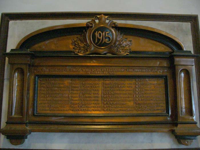 A bronze memorial tablet in a wooden frame, headed with the date 1915 in a wreathed cartouche, inscribed to the memory of those killed during the mutiny in Singapore in February 1915, with columns of names below.