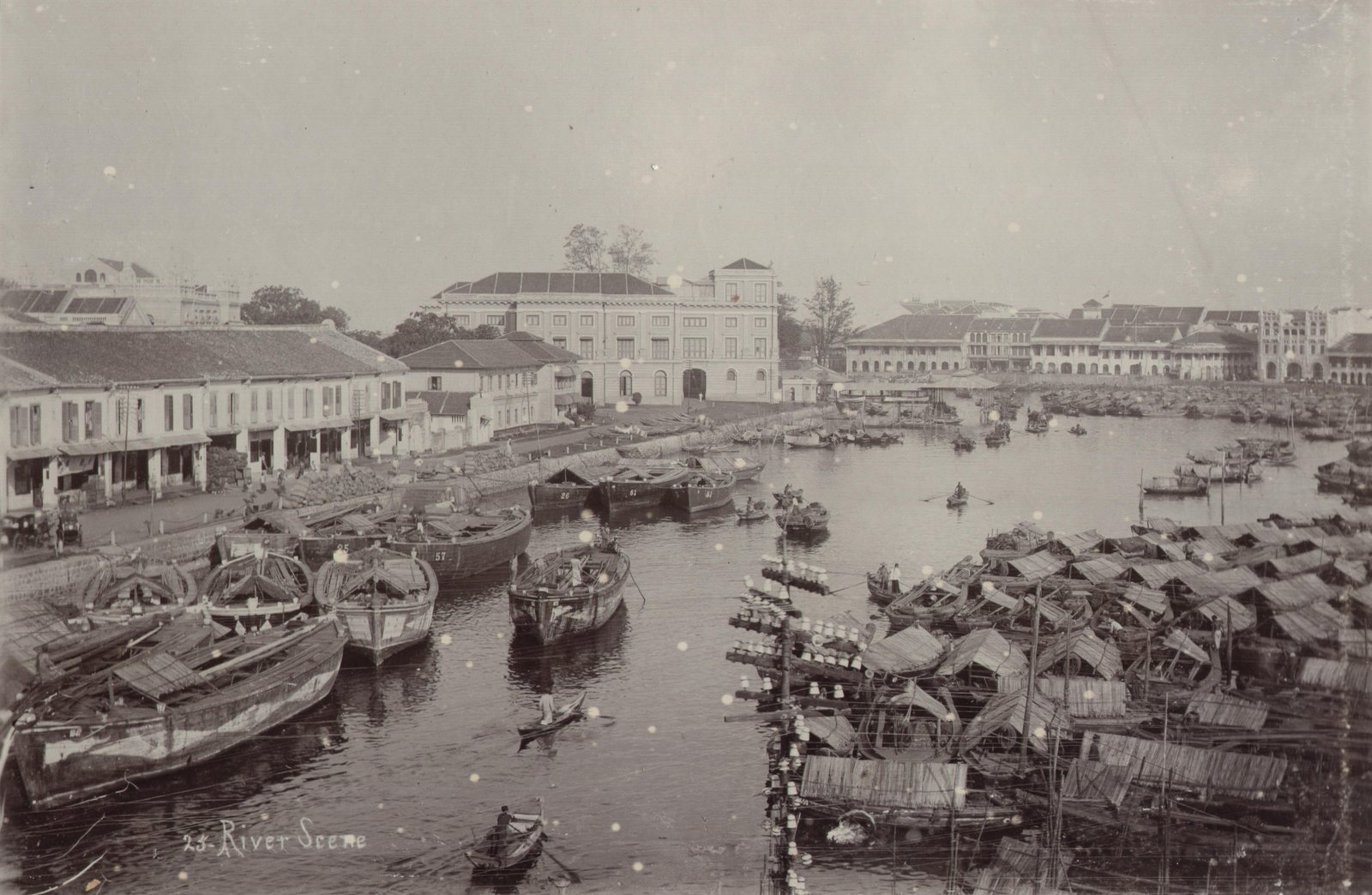 The port of Singapore about 1900: the river packed bank to bank with lighters and covered boats, shophouses and godowns along the left-hand quay, and a large colonnaded building facing the water.